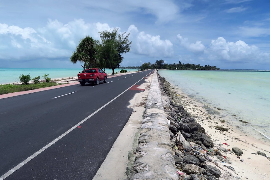 A new-looking bitumen road connecting one island to another, with a build-up of sand and rocks on either side.