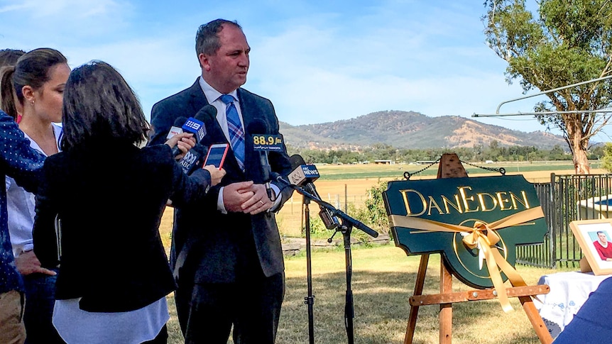 Man standing at microphones in front of him in a farm setting