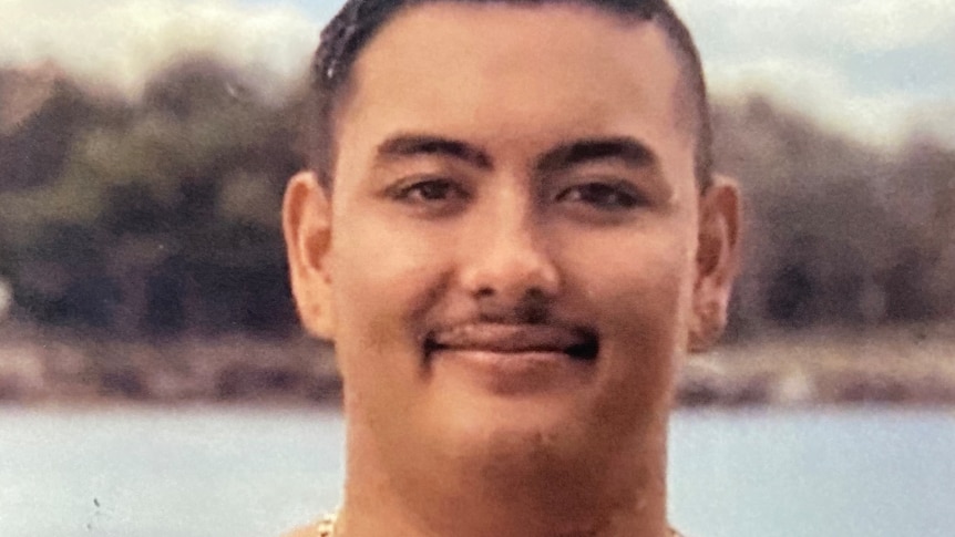 A portrait shot of a shirtless and smiling Jesse Vikelis-Curas, wearing a thick gold necklace.