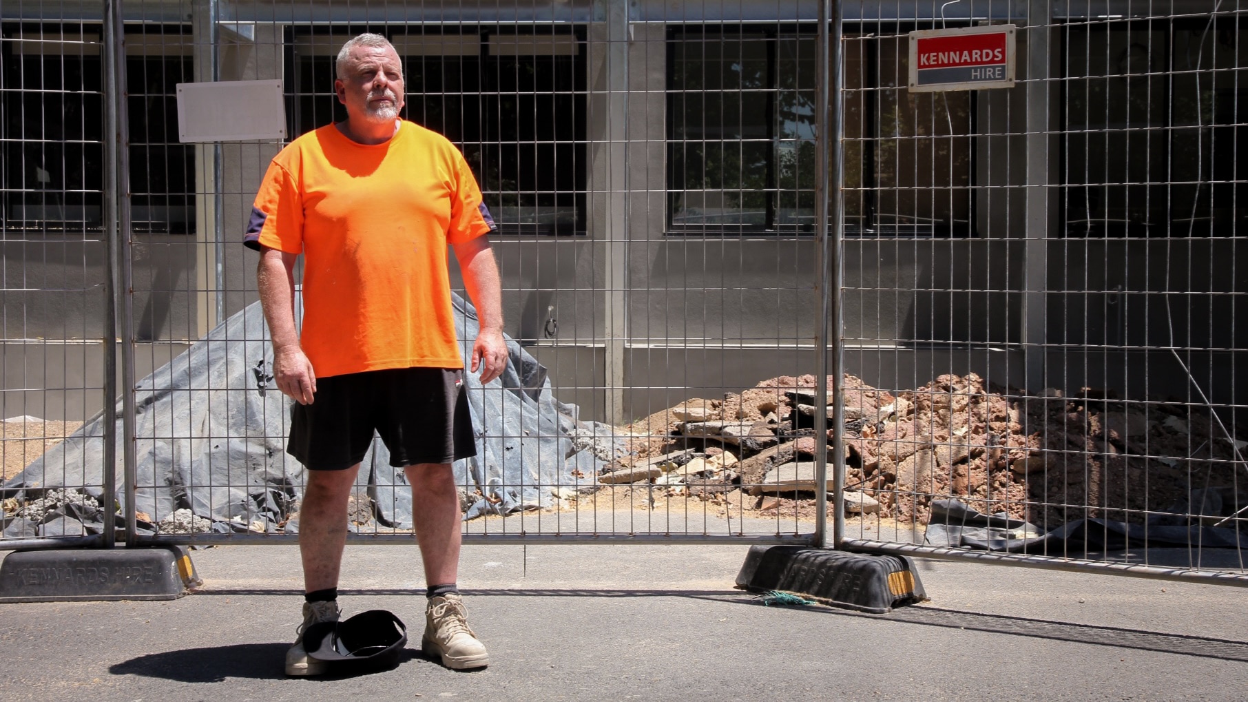 A middle-aged man in an orange hi-vis shirt standing in front of a construction site.