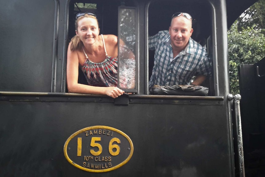 A couple lean out of a train, smiling.