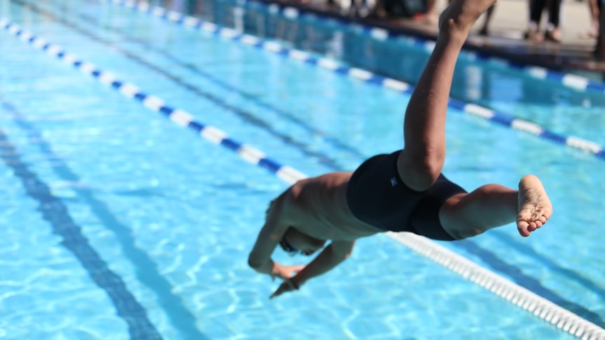 A young man in black swimming shorts dives into a pool