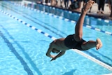 A young man in black swimming shorts dives into a pool.