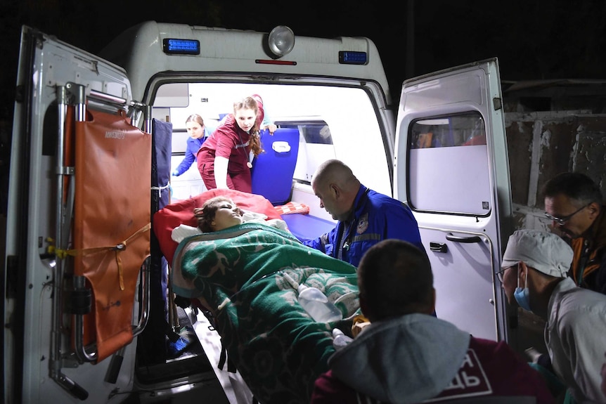 A young victim of the Crimea college attack is being loaded into an ambulance with paramedics supporting her.
