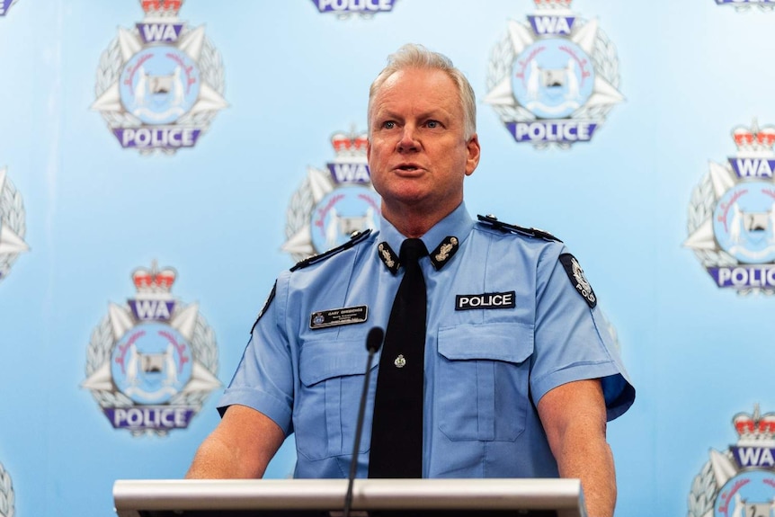 Gary Dreibergs in uniform standing at a podium at a press conference in front of WA Police logos