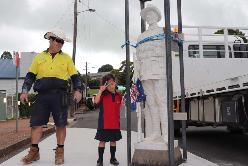Workman with a schoolgirl stands next to a statue of a marble soldier