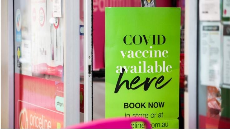 A sign in a window reading covid vaccine available here book now