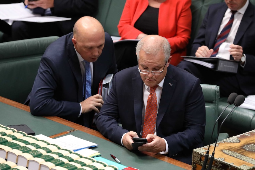 Peter Dutton looks over Scott Morrison's shoulder as they read from the PM's mobile phone