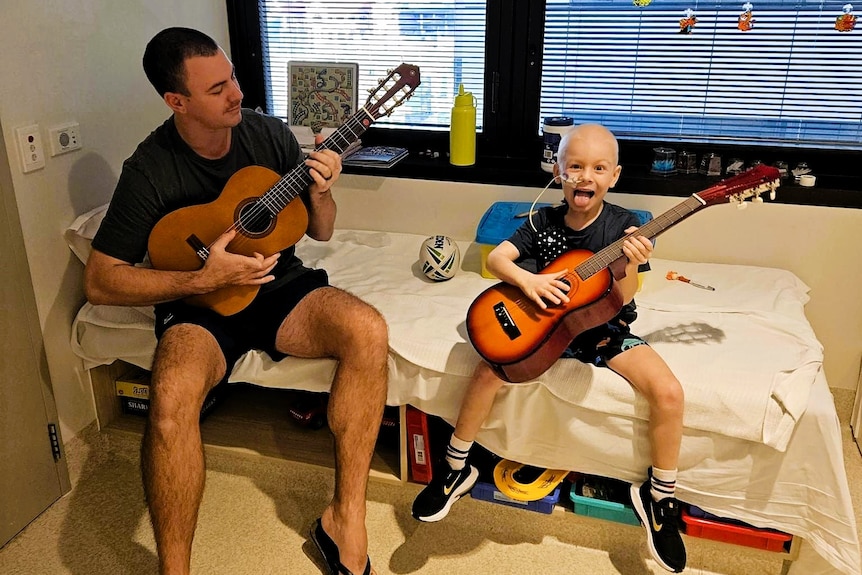 A man and a young boy sitting on a hospital bed.  They are both holding guitars