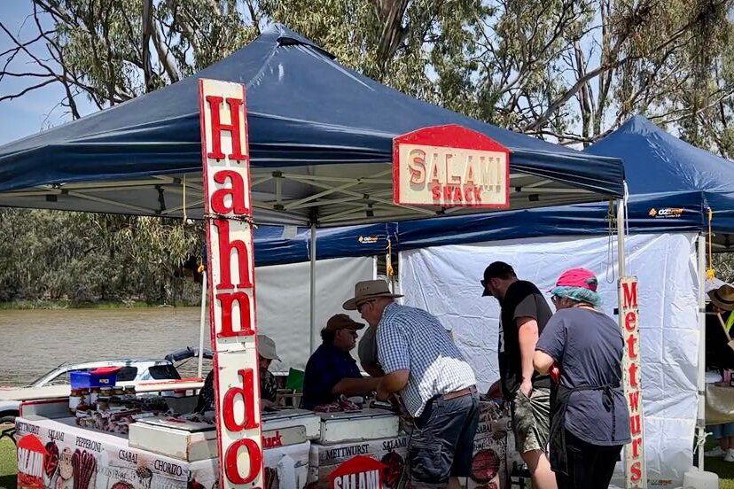 Pit tent market stall with makers selling salami in front of the Murray River