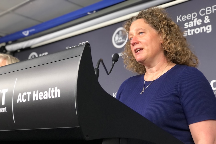 A woman with curly hair speaks into a microphone.