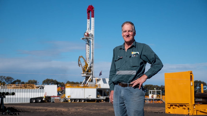 A farmer stands near gas drilling rig on his property.