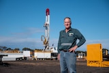 A farmer stands near gas drilling rig on his property.