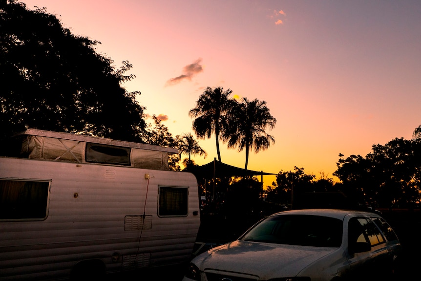 A car and caravan with tropical sunset, palm trees in the background.