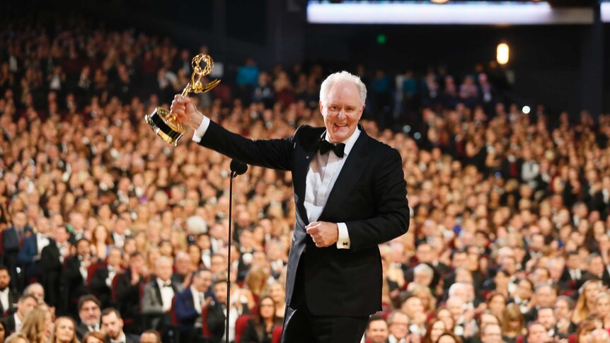 Veteran actor John Lithgow holds his 2017 emmy award on stage.