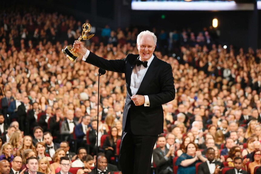 Veteran actor John Lithgow holds his 2017 emmy award on stage.