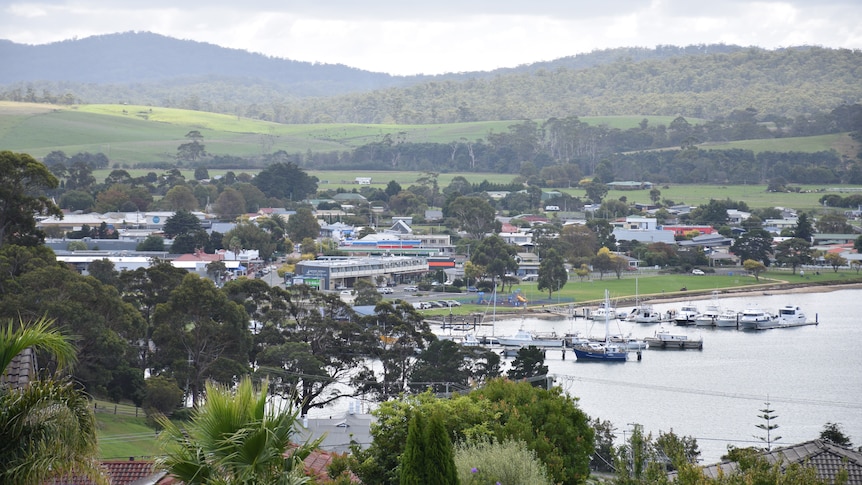 A landscape shows a town by the water, with boats bobbing in the sea.