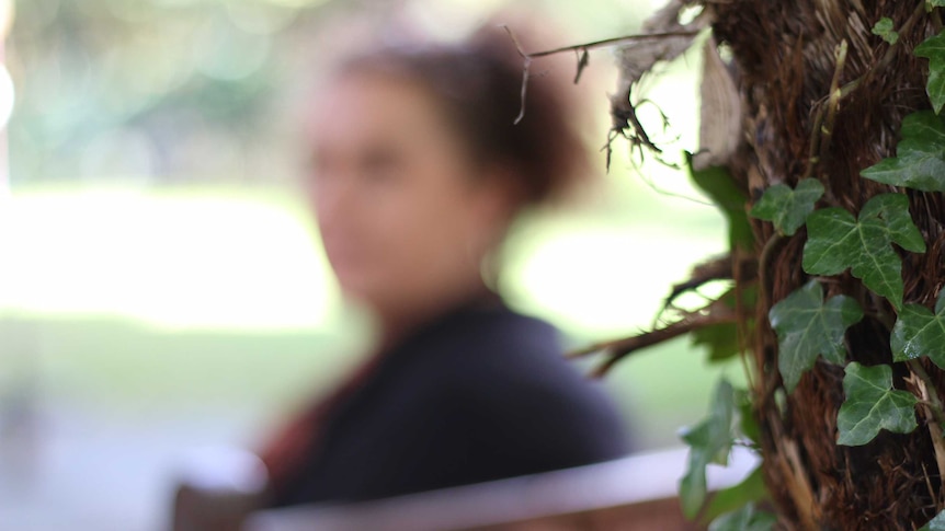Blurred photo of domestic violence survivor 'J', with foliage in the foreground in focus.