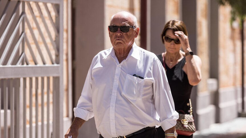 An older man in a white business shirt walks along a footpath.
