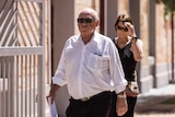 An older man in a white business shirt walks along a footpath.