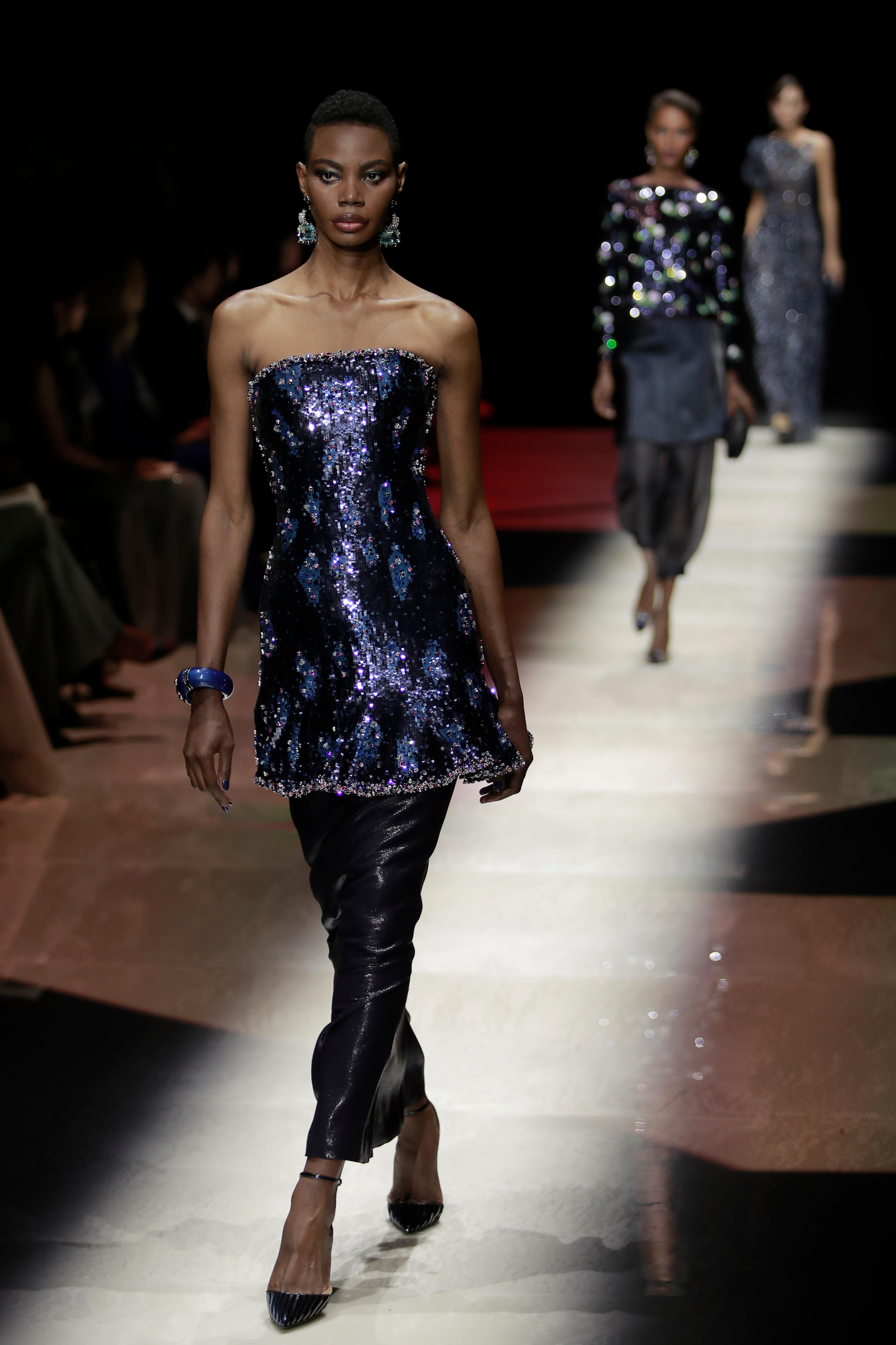 A model wears a blue sequin dress over shiny black pants. 
