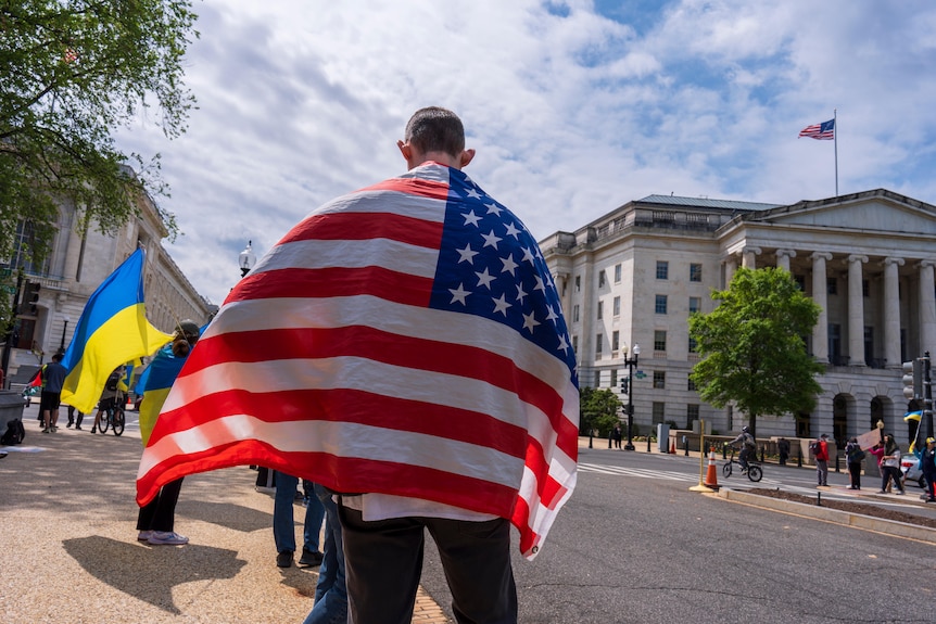 The back of a man covered in a us flag with people carrying ukraine flags
