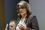A Caucasian woman with brown hair, wearing glasses and a blazer.