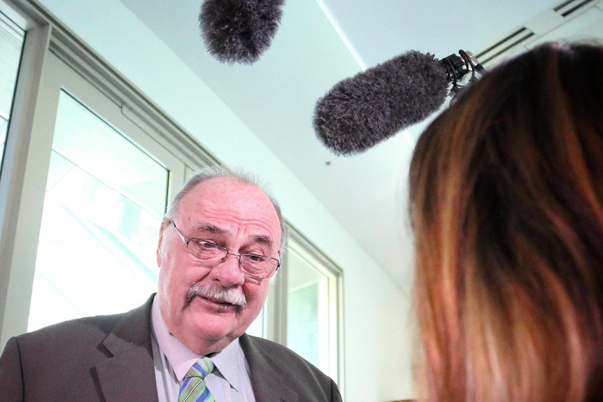 Warren Entsch speaks to a reporter with boom microphones above his head