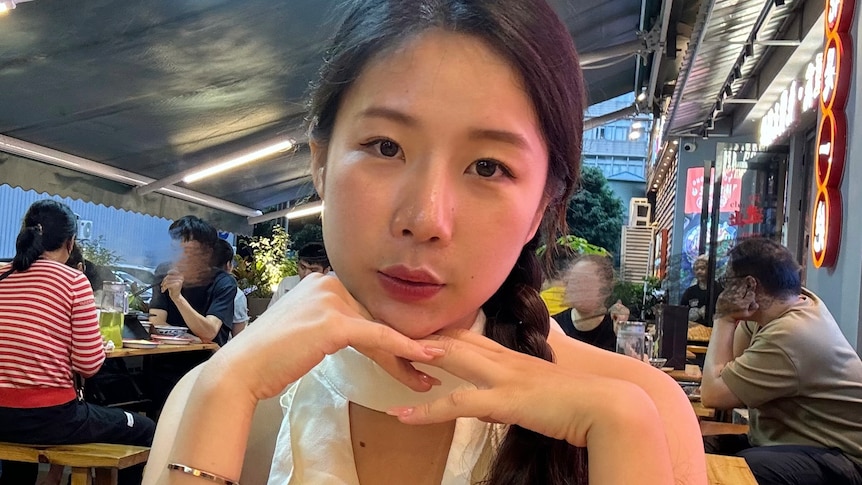 Lin Zijuan sitting with her chin on her hands in a restaurant. 