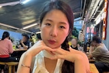 Lin Zijuan sitting with her chin on her hands in a restaurant. 
