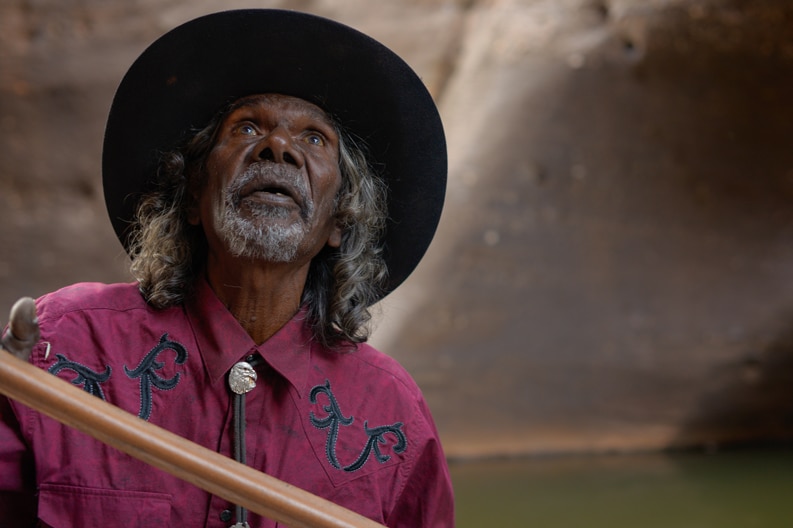 A still showing Dalaithngu wearing a wide hat.