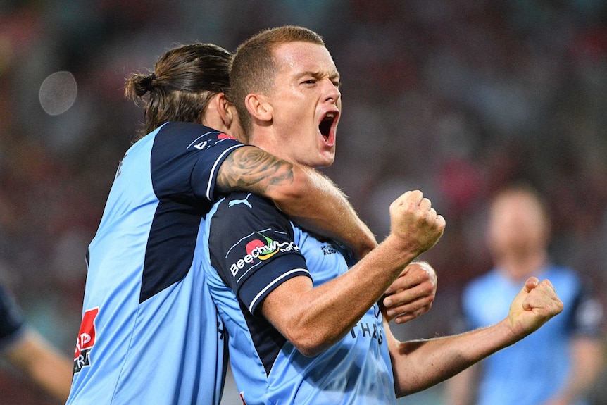 Brandon O'Neill pumps his fists while being hugged by a Sydney FC teammate after scoring a goal.