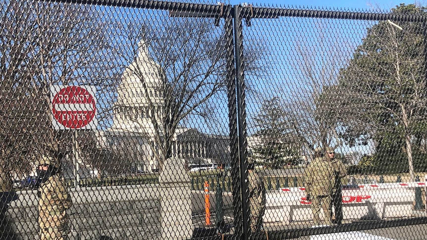 Men dressed in army uniforms and wearing masks stand inside a chained fence around the Capitol.