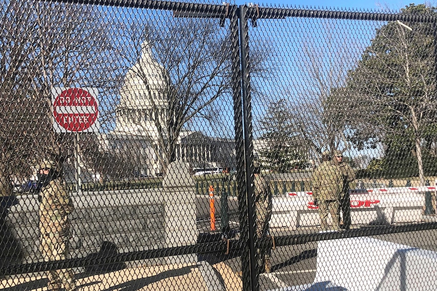 Men dressed in army uniforms and wearing masks stand inside a chained fence around the Capitol.