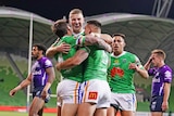 A group of NRL teammates hug in celebration after scoring a try.