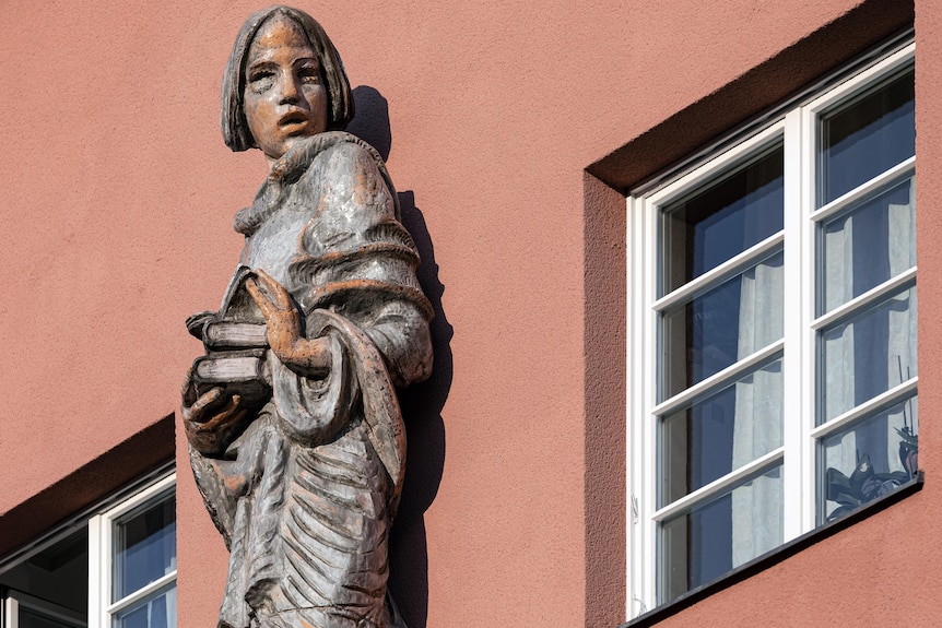 A large statue of a woman fixed to the front of a red apartment building.