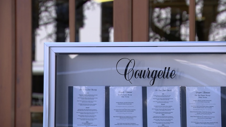A glass sign, which reads 'Courgette', holding a menu inside.