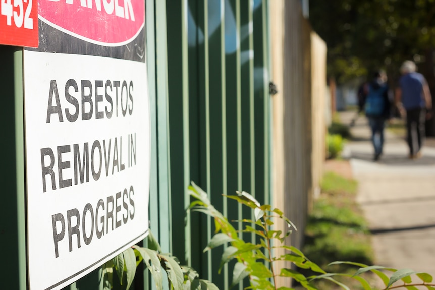 Removalist Roden Woodhams and reporter Mario Christodoulou walk past a sign that warns asbestos is being removed in the area