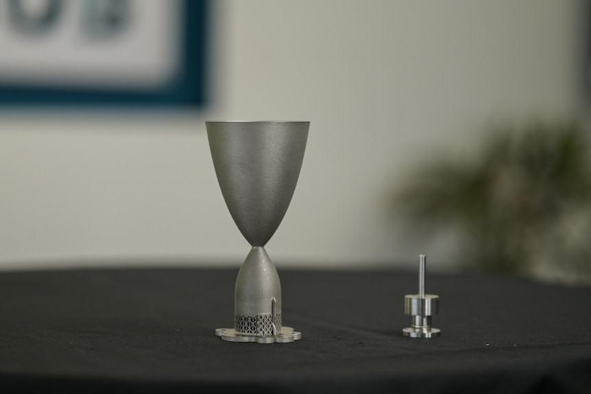 The thruster, which looks like a small trophy, and a valve on a black table.