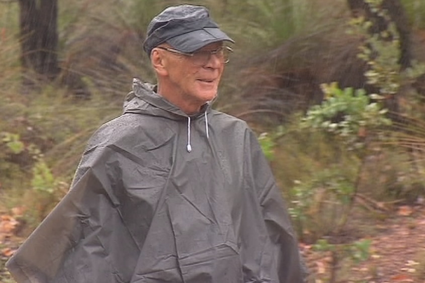 A hiker wearing a black rain poncho walks through bushland.