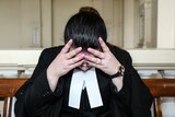 A stressed out lawyer in her robes holding her head in her hands.