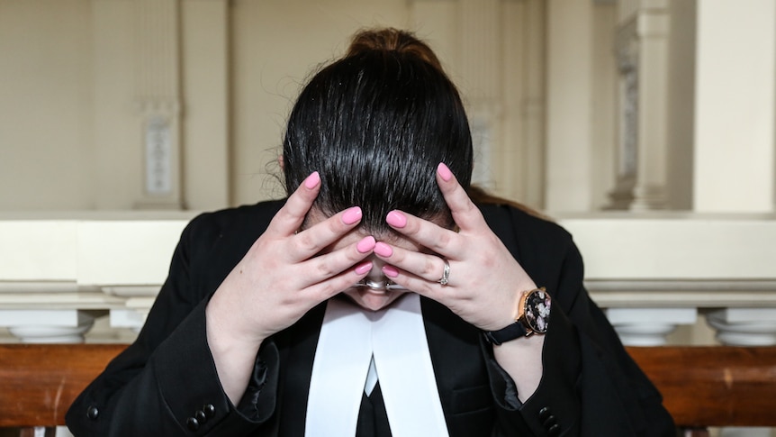 A stressed out lawyer in her robes holding her head in her hands.