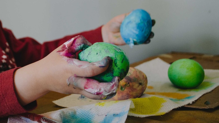 A little boy holds a green blob of plasticine in one hand and a blue blob in the other.