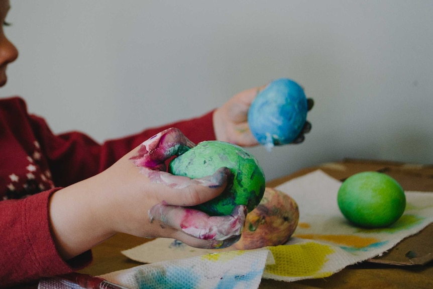 A little boy holds a green blob of plasticine in one hand and a blue blob in the other.