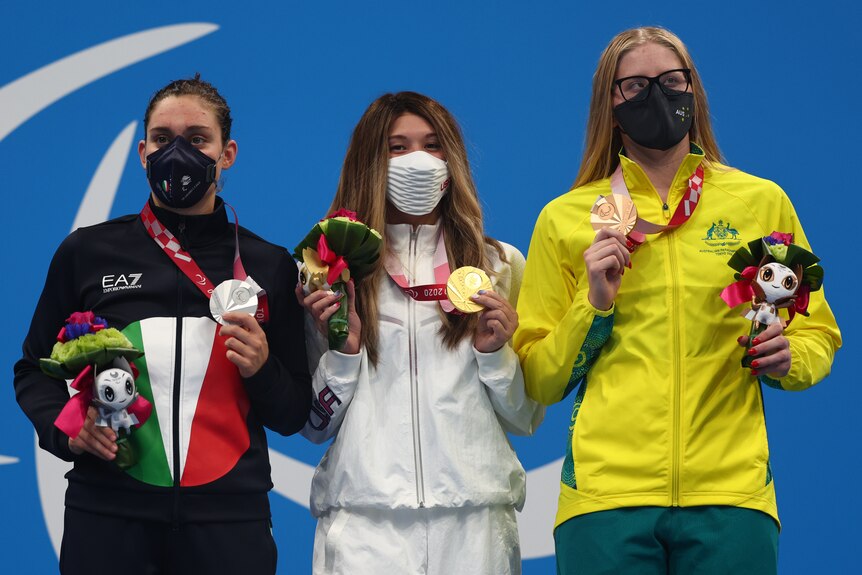 Three female swimmers hold up their medals on the podium at the Tokyo Paralympics.