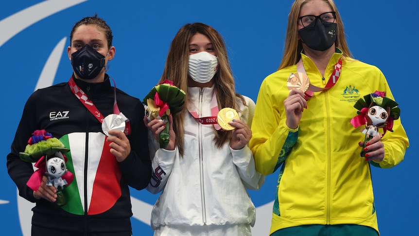 Three female swimmers hold up their medals on the podium at the Tokyo Paralympics.