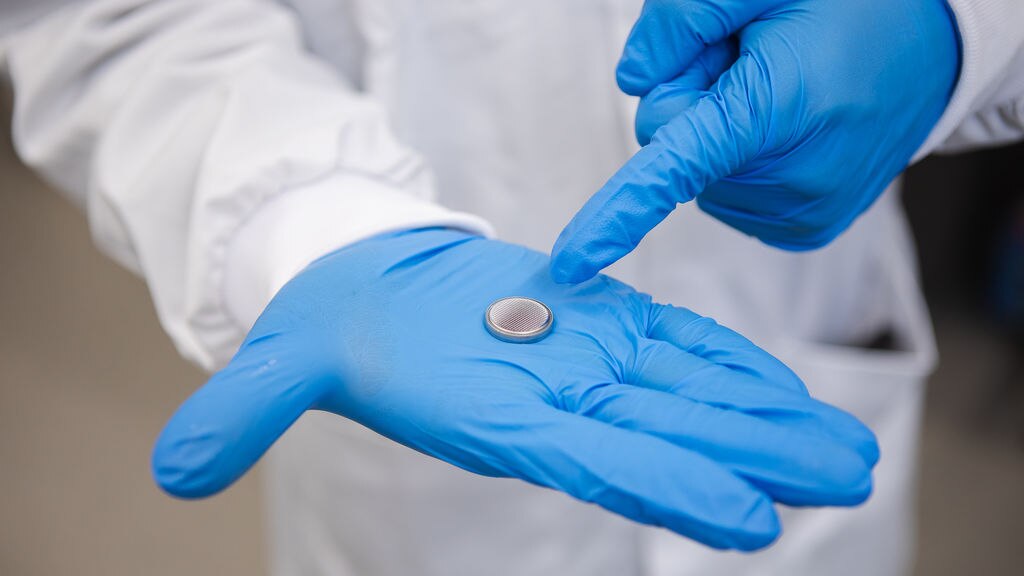 Researcher indicating at water battery sitting in gloved hands