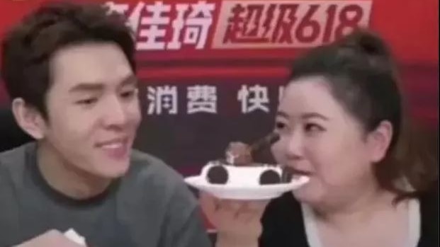 Two people look at a tank-like cake. 