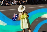 A young girl in a yellow dress holds a small Australian flag on the side of a street