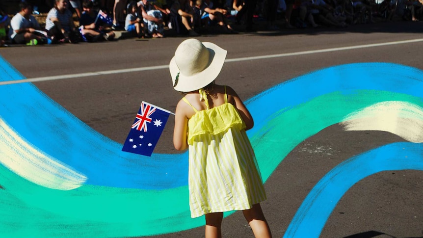 A young girl in a yellow dress holds a small Australian flag on the side of a street